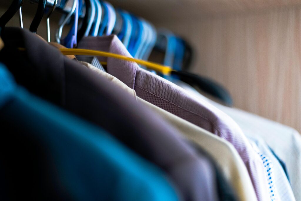 Close-up of various shirts hanging on colorful hangers inside a wardrobe.